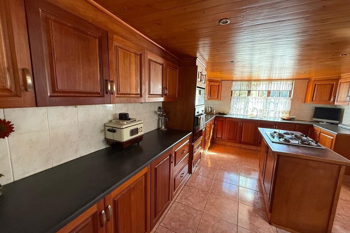 A traditional kitchen featuring solid wood cabinetry, dark countertops, a central island with a built-in gas hob, and a warm timber-clad ceiling.