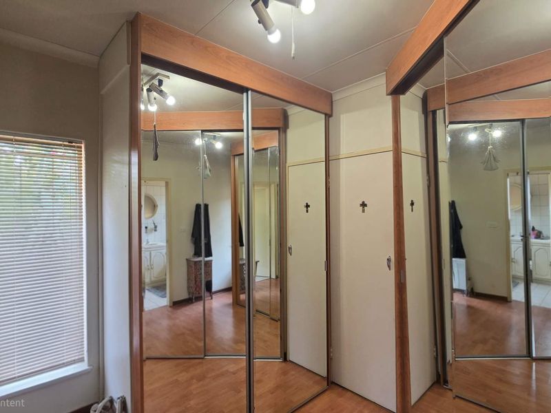 Bedroom featuring built-in mirrored wardrobes and laminate flooring, offering a functional space with natural light from the window.