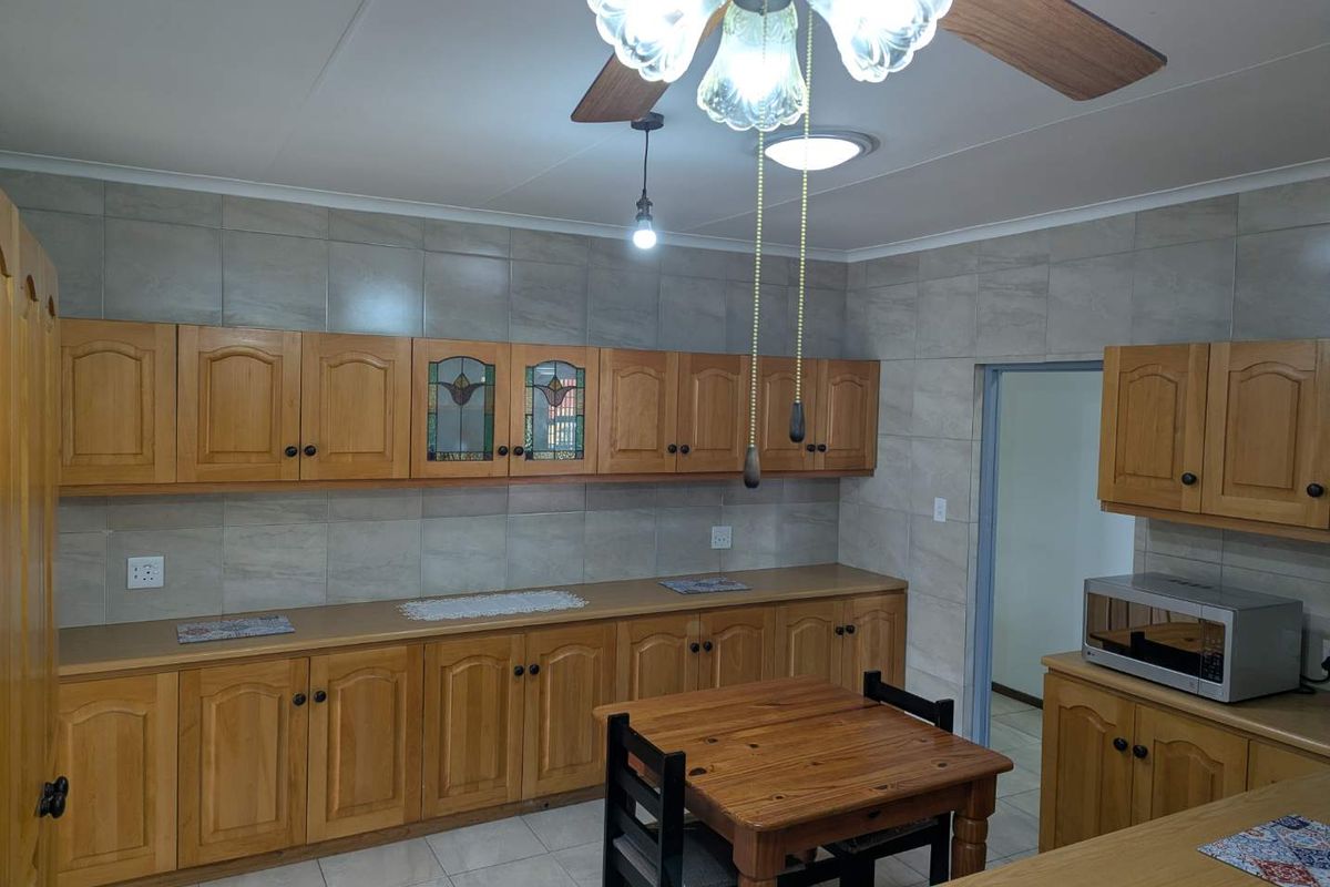 A functional kitchen featuring extensive wooden cabinetry, tiled backsplash, and tiled flooring, illuminated by a ceiling fan and pendant lighting.