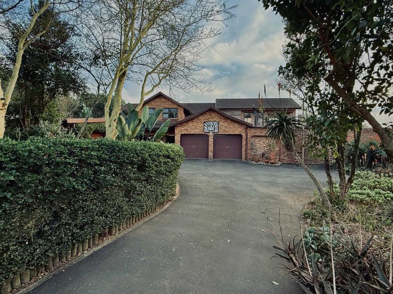 Front view of a double-story brick house featuring a double garage, paved driveway, and established garden surroundings.