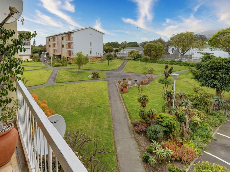 Elevated view from a balcony overlooking a well-maintained communal garden area with paved pathways and surrounding apartment buildings.