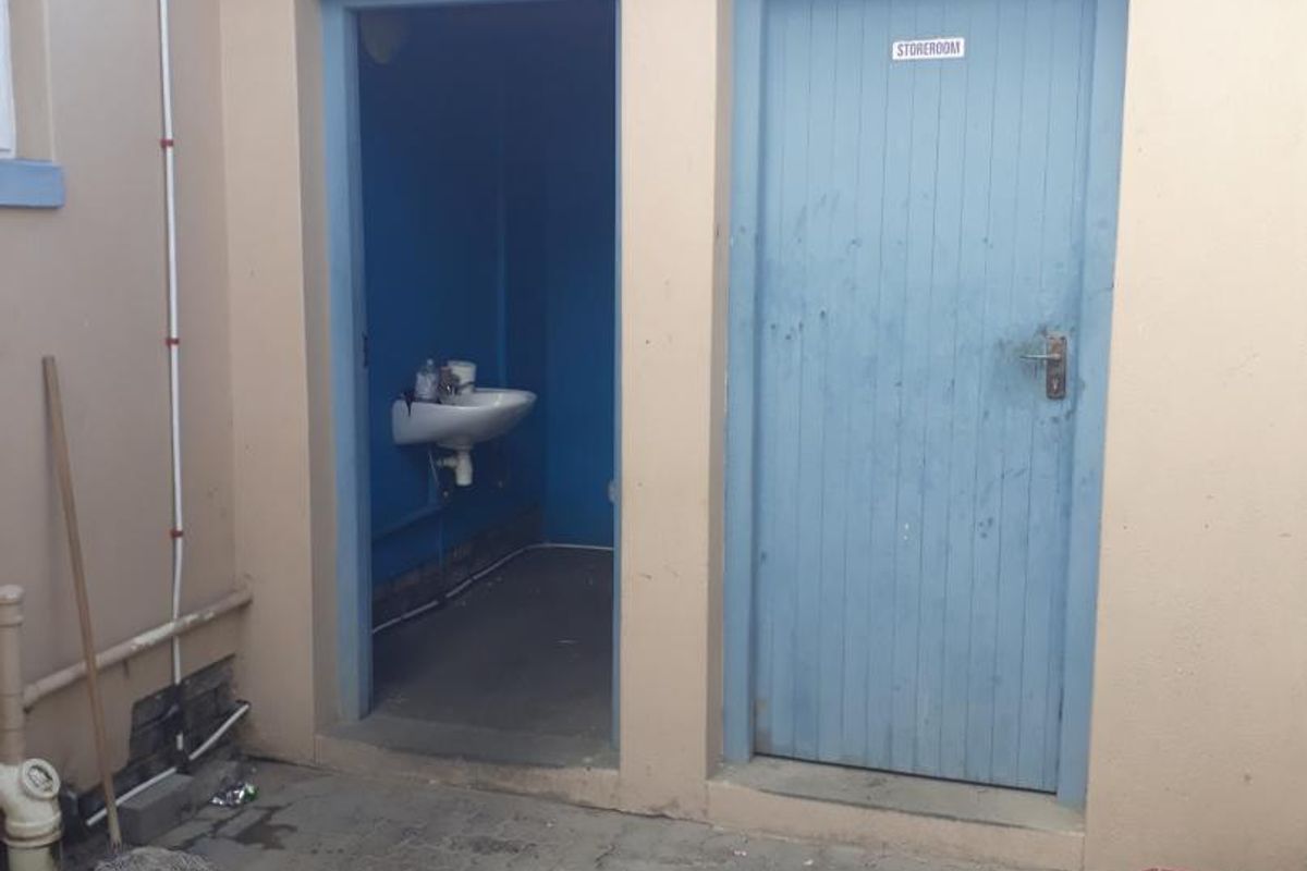 Exterior view of a utility area featuring a small washroom with a basin and an adjacent storeroom with a blue wooden door.
