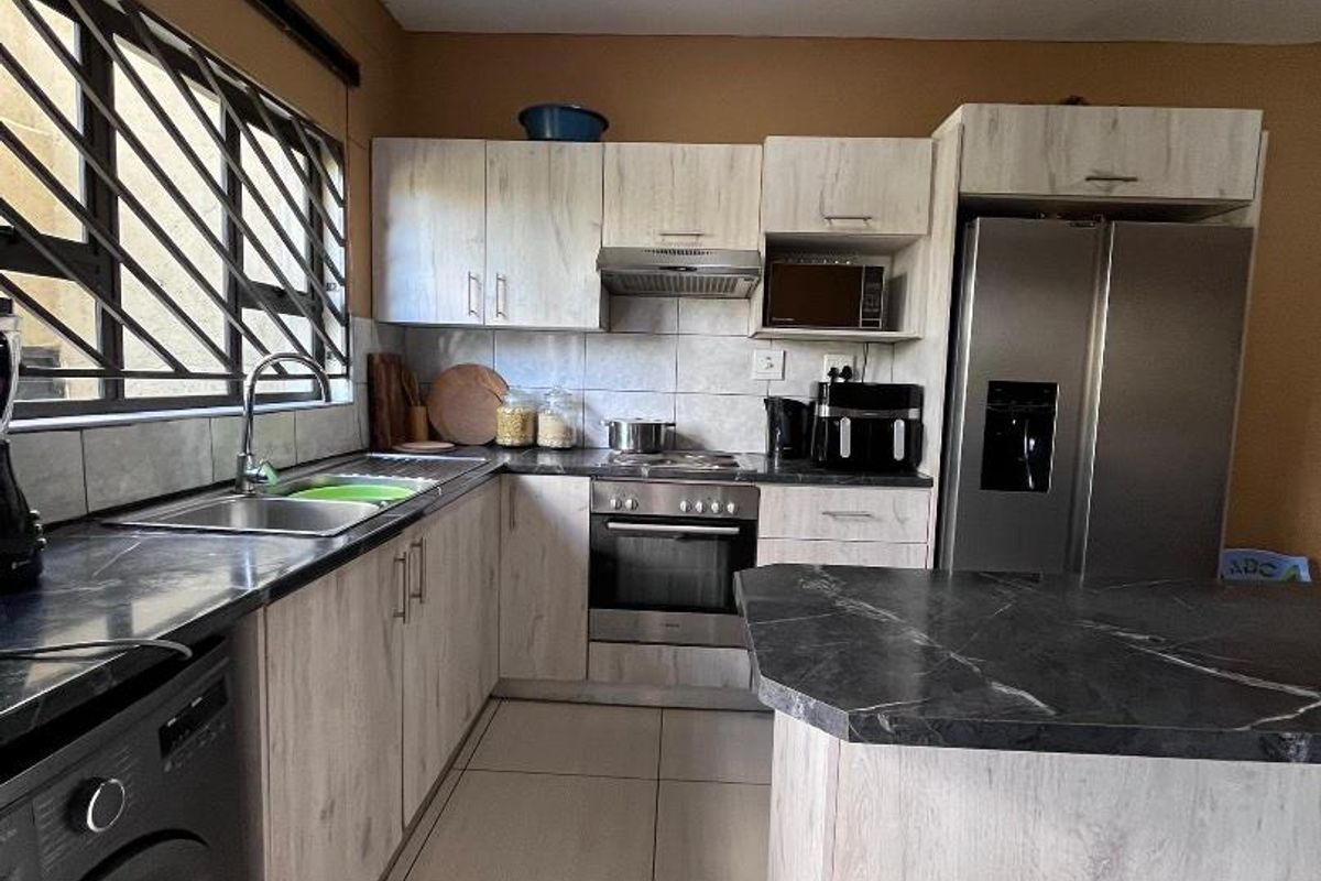 Functional kitchen featuring light wood-grain cabinetry, dark stone-look countertops, integrated oven, extractor fan, and tiled flooring.