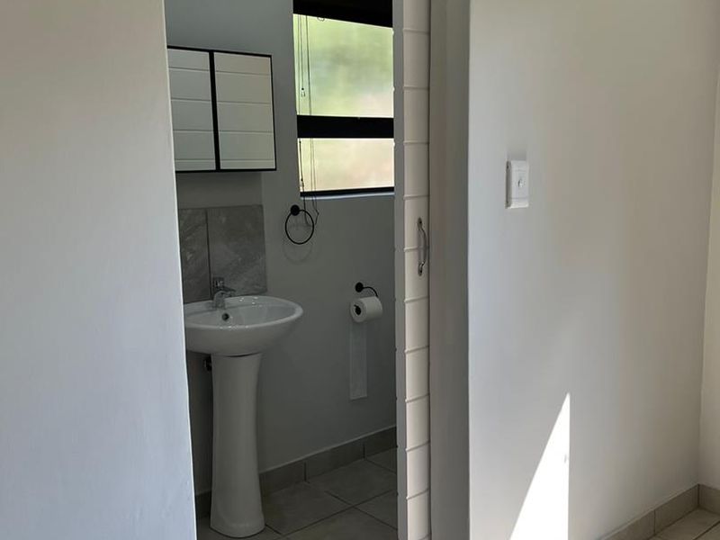 A clean, minimalist bathroom featuring a pedestal sink, tiled flooring, and a sliding door entry, presenting a well-maintained and functional space.