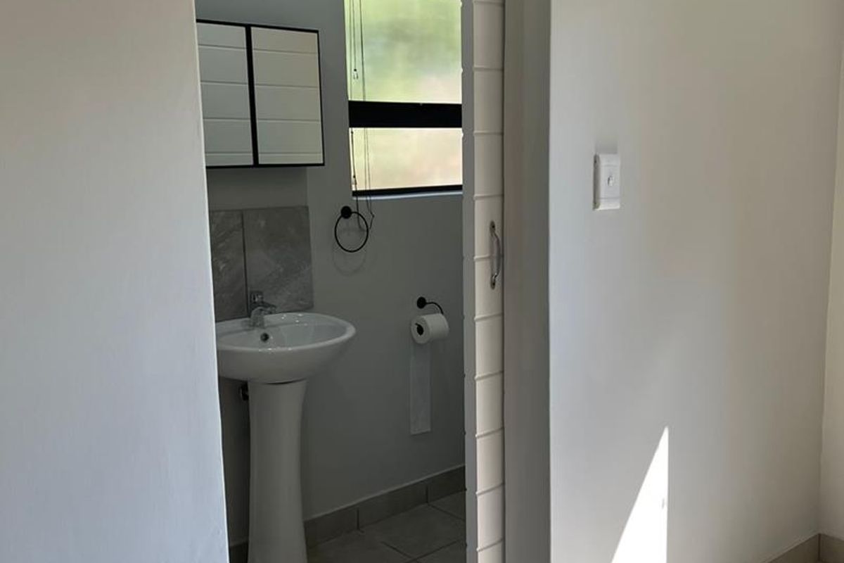 A clean, minimalist bathroom featuring a pedestal sink, tiled flooring, and a sliding door entry, presenting a well-maintained and functional space.