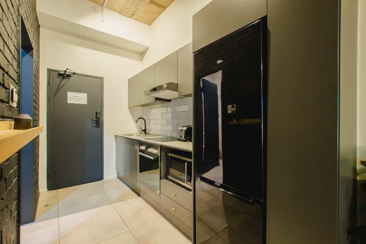 Modern galley-style kitchen featuring sleek grey cabinetry, integrated appliances, subway tile backsplash, and a striking exposed brick wall.