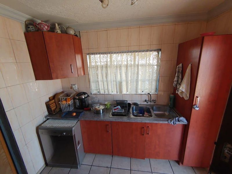A compact kitchen featuring laminate cabinetry, a double basin sink, and tiled wall finishes, offering a functional layout in need of cosmetic updates.