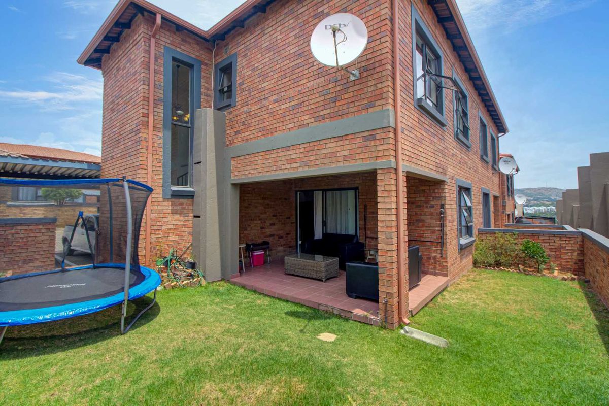 A rear view of the townhouse featuring a covered patio with tiled flooring, brick exterior walls, and a private garden area.