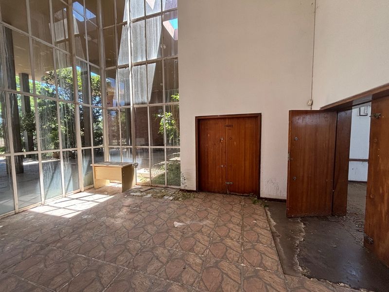 Spacious office area featuring floor-to-ceiling glass windows, tiled flooring, and wooden doors, requiring significant maintenance and refurbishment to restore its professional appeal.