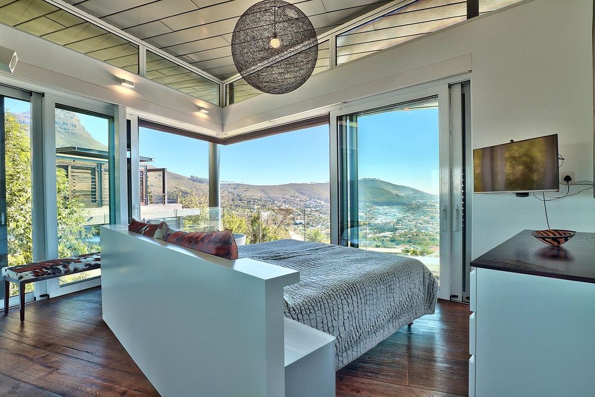 Modern bedroom featuring expansive floor-to-ceiling windows, hardwood flooring, and panoramic mountain views with a contemporary open-plan layout.