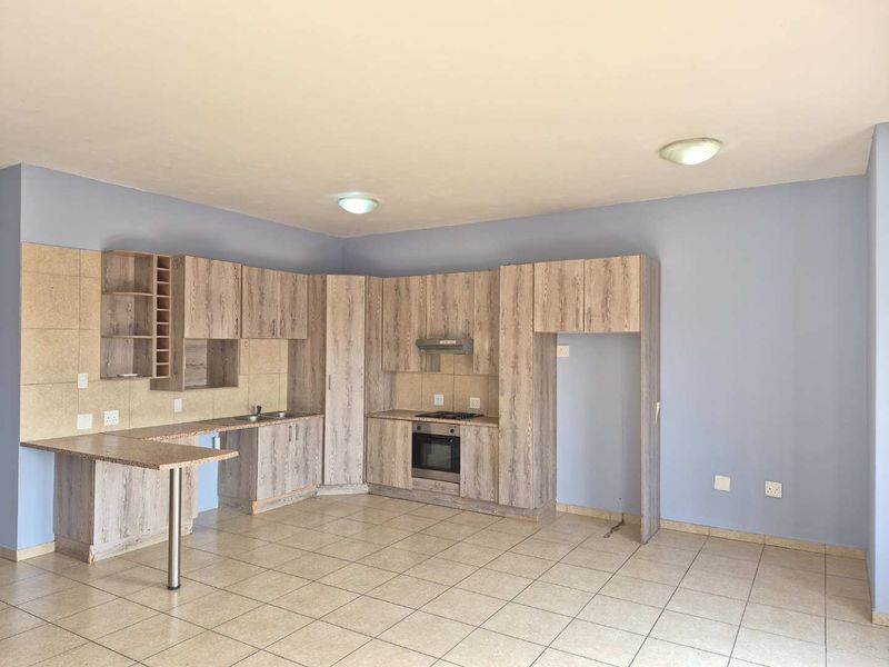 An open-plan kitchen featuring wood-look cabinetry, built-in oven and hob, tiled flooring, and a breakfast bar extension.