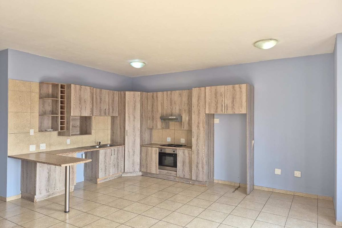 An open-plan kitchen featuring wood-look cabinetry, built-in oven and hob, tiled flooring, and a breakfast bar extension.