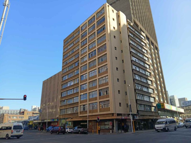 A street-level view of a multi-story apartment building featuring a grid-pattern facade and ground-floor commercial spaces in an urban setting.