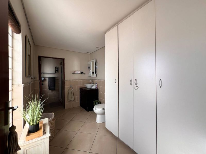 A spacious bathroom featuring extensive built-in storage cupboards, a vanity with a vessel sink, and neutral tiled finishes throughout.