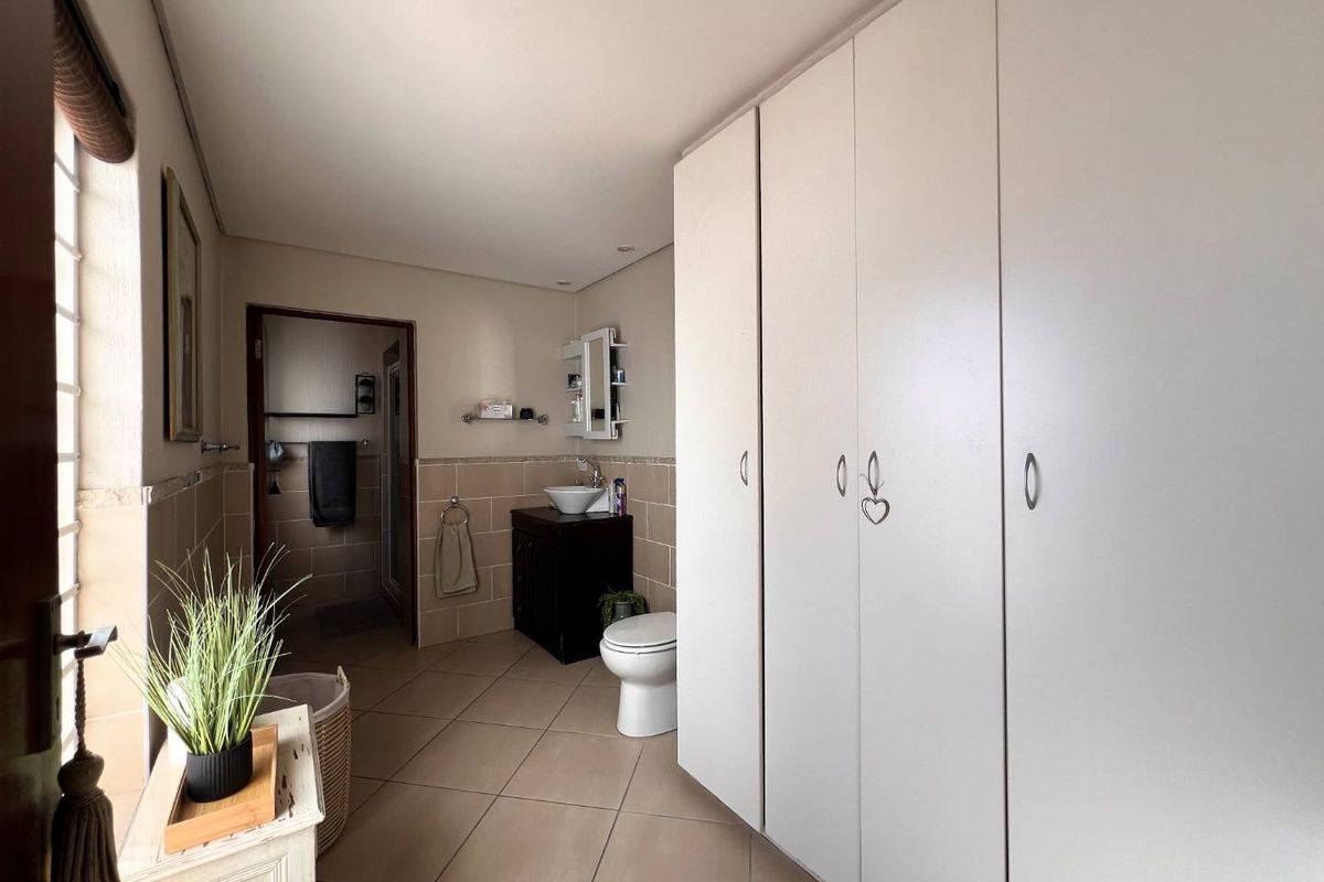 A spacious bathroom featuring extensive built-in storage cupboards, a vanity with a vessel sink, and neutral tiled finishes throughout.
