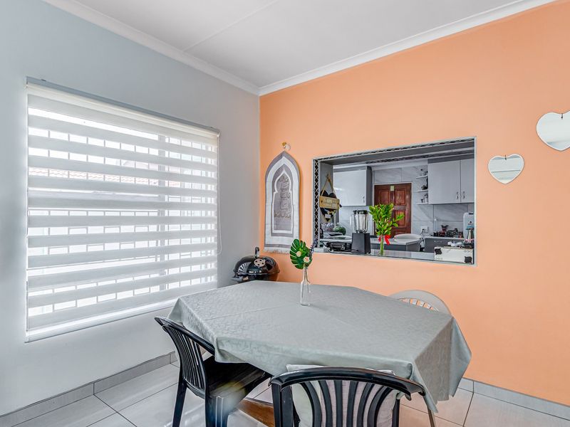 Dining area featuring tiled flooring, a convenient pass-through window to the kitchen, and modern roller blinds.