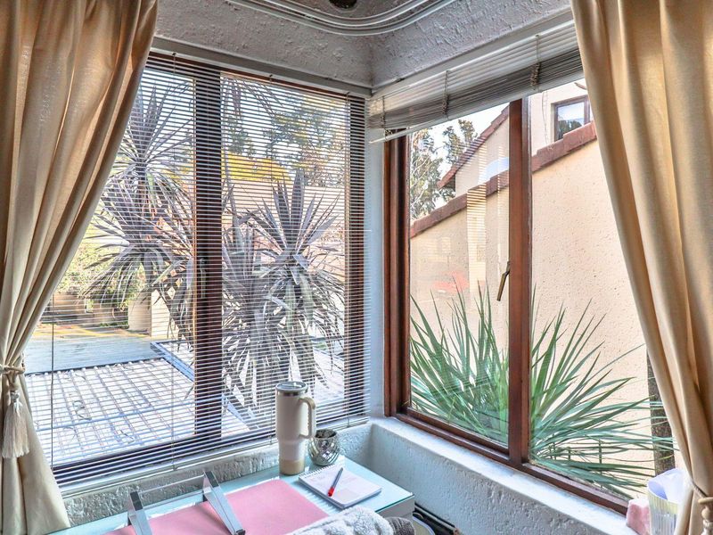 A sunlit corner space featuring large timber-framed windows with integrated blinds, offering views of the outdoor area.