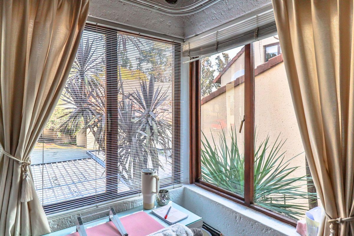 A sunlit corner space featuring large timber-framed windows with integrated blinds, offering views of the outdoor area.