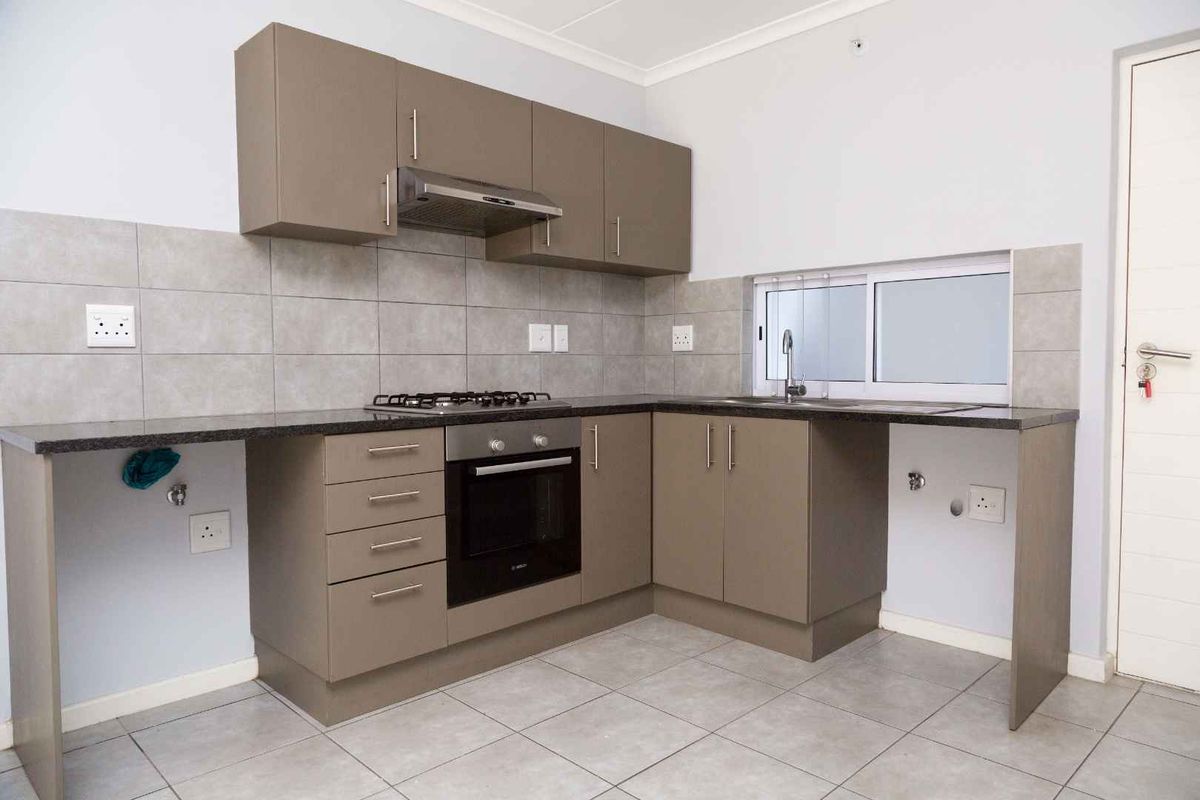 Modern kitchen featuring taupe cabinetry, granite countertops, built-in oven, gas hob, extractor fan, and tiled splashbacks.