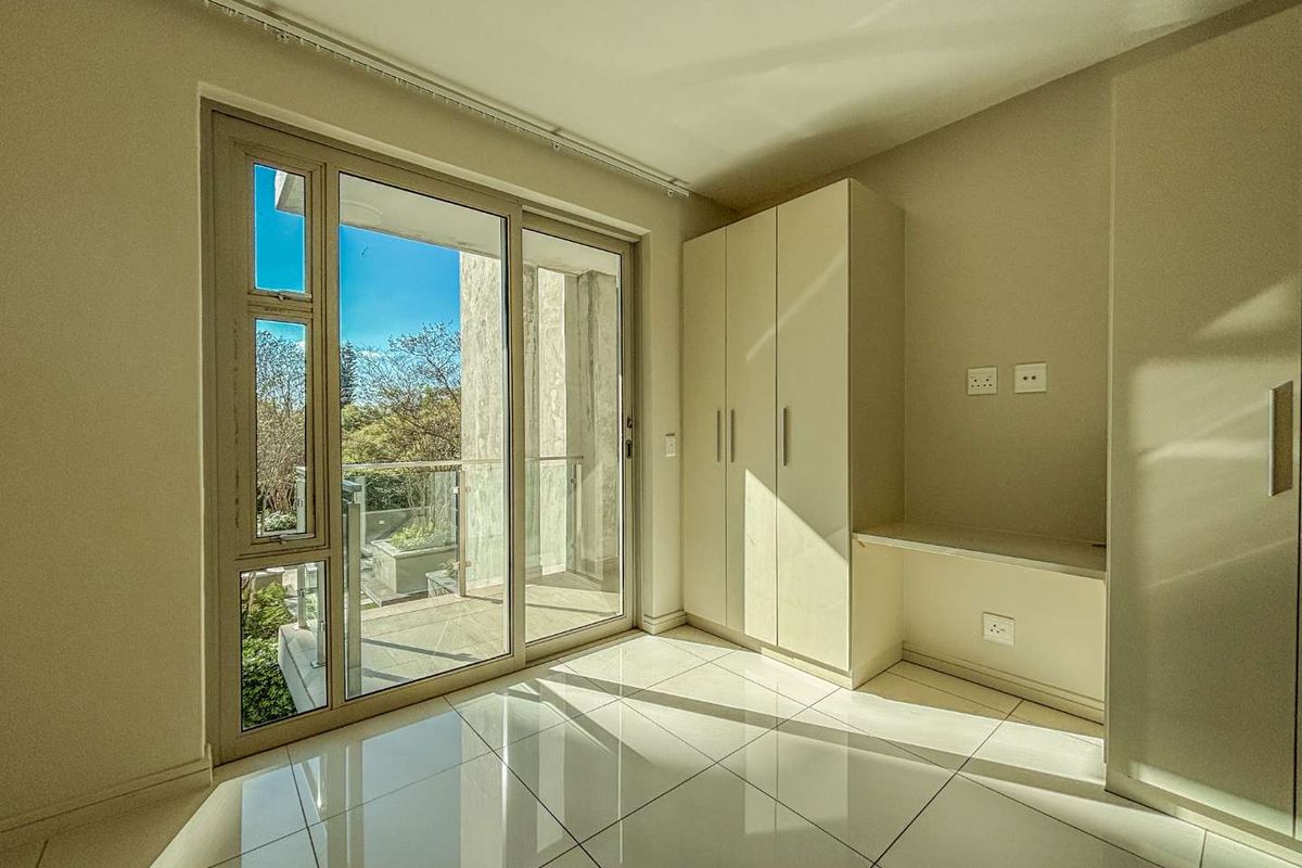 A bright bedroom featuring built-in cabinetry, a desk area, tiled flooring, and large sliding glass doors opening onto a private balcony.