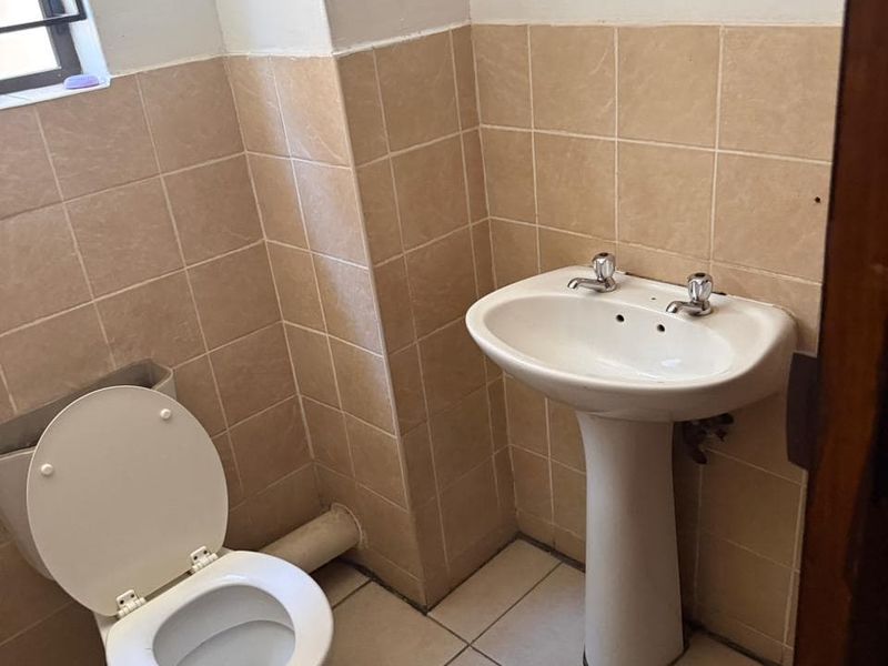 A compact bathroom featuring a pedestal basin and toilet with neutral ceramic wall and floor tiling, requiring minor cosmetic updates.