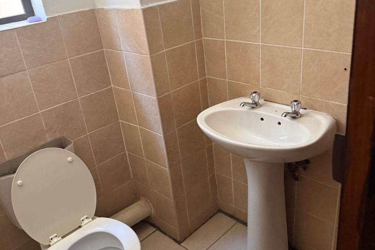 A compact bathroom featuring a pedestal basin and toilet with neutral ceramic wall and floor tiling, requiring minor cosmetic updates.