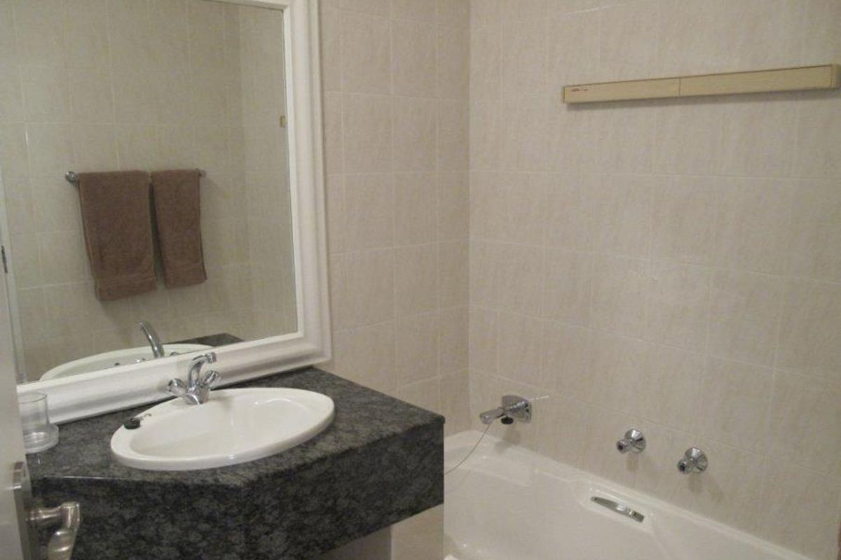 A functional bathroom featuring a granite-topped vanity with an inset basin, a wall-mounted mirror, and a standard bathtub with chrome fixtures.
