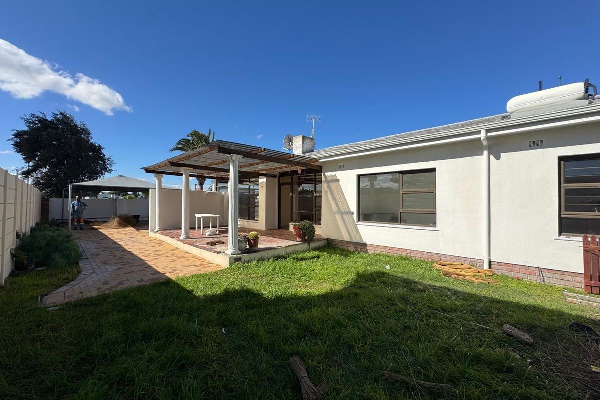 Rear view of the property featuring a covered patio area, paved walkway, and a spacious garden with established lawn.