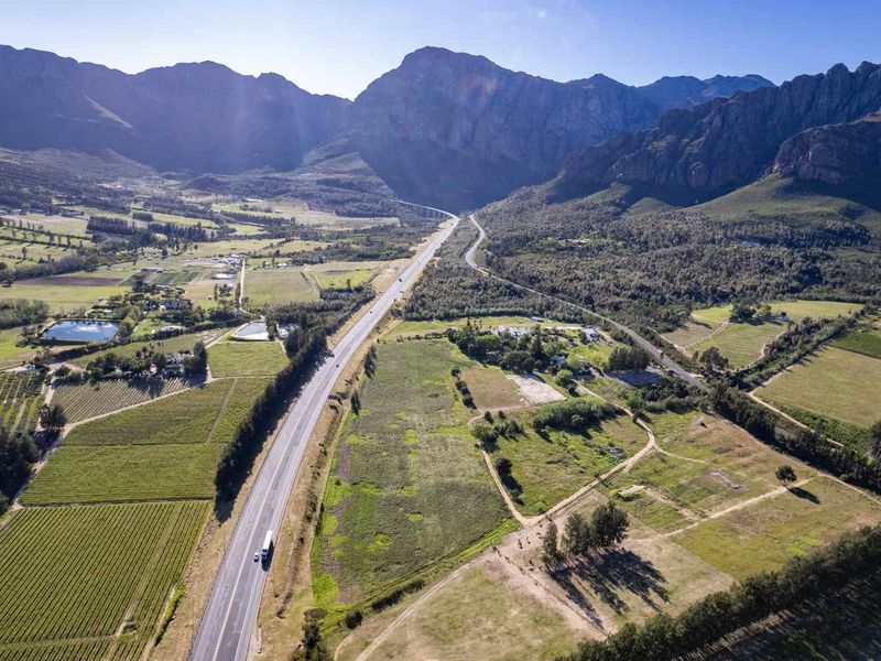 An expansive aerial view of the farm property, showcasing surrounding vineyards, open agricultural land, and proximity to the mountain range and highway.