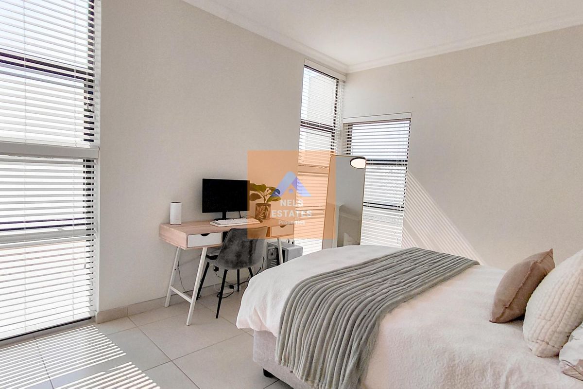 A bright and modern bedroom featuring large windows with venetian blinds and neutral tiled flooring.