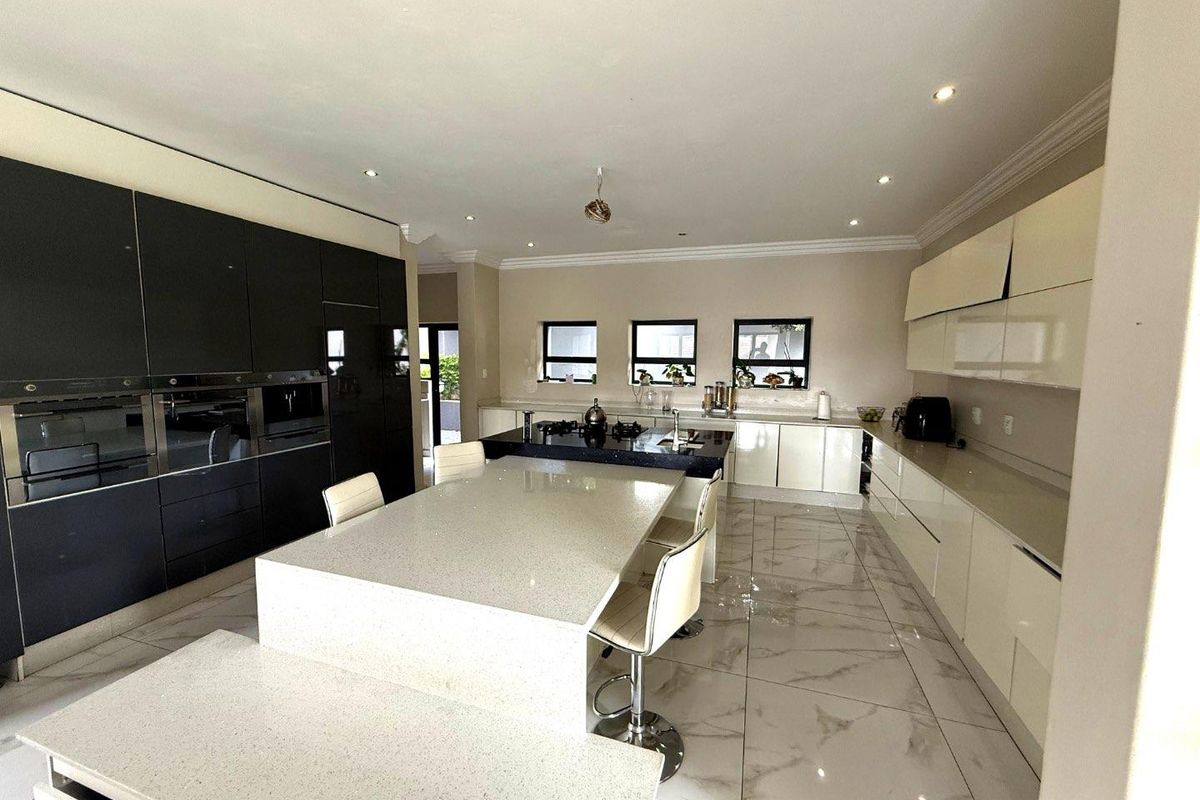 Modern kitchen featuring high-gloss cabinetry, a large central island with stone countertops, integrated appliances, and polished marble-look floor tiles.