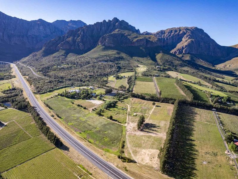 An expansive aerial view of a large farm property featuring extensive agricultural land, vineyards, and a scenic mountain backdrop.