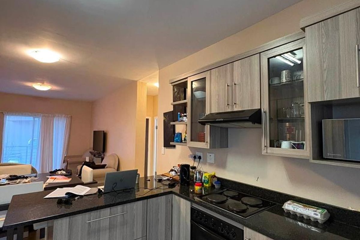 Open plan kitchen featuring modern wood-look cabinetry, granite countertops, and integrated appliances, flowing seamlessly into the adjacent living area.