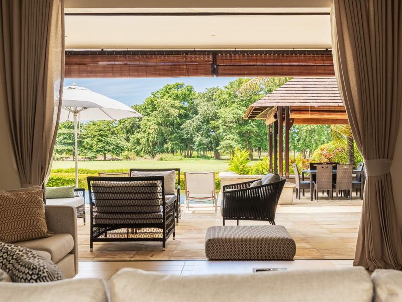A seamless transition from the indoor living area to a spacious covered patio, featuring natural stone flooring and views of the garden.