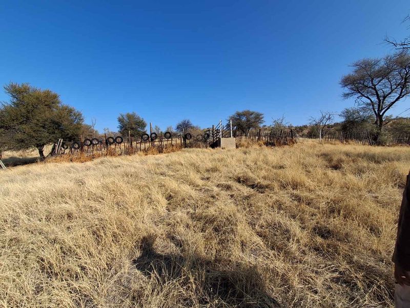 Expansive open land area featuring a wire fence boundary and a small concrete structure, set within a rural small holding landscape.