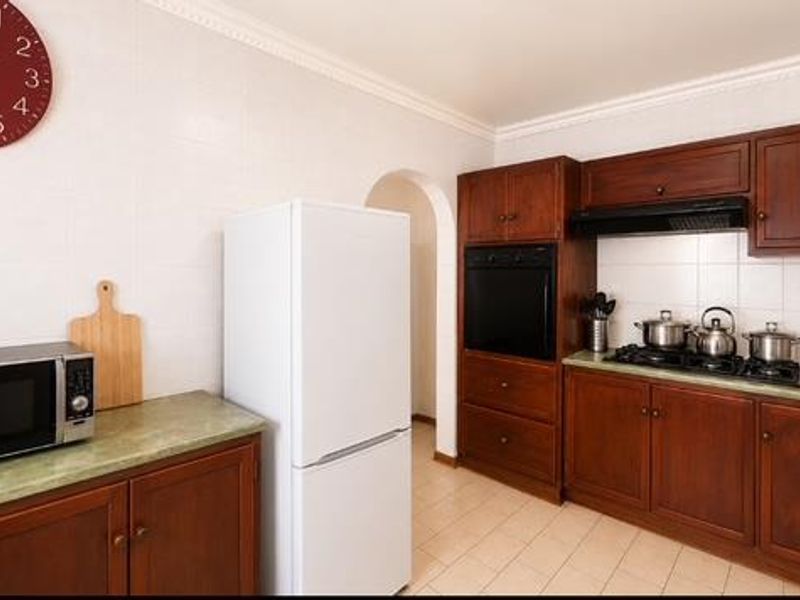 A functional kitchen featuring dark wood cabinetry, built-in oven, gas hob with extractor fan, and tiled finishes throughout.