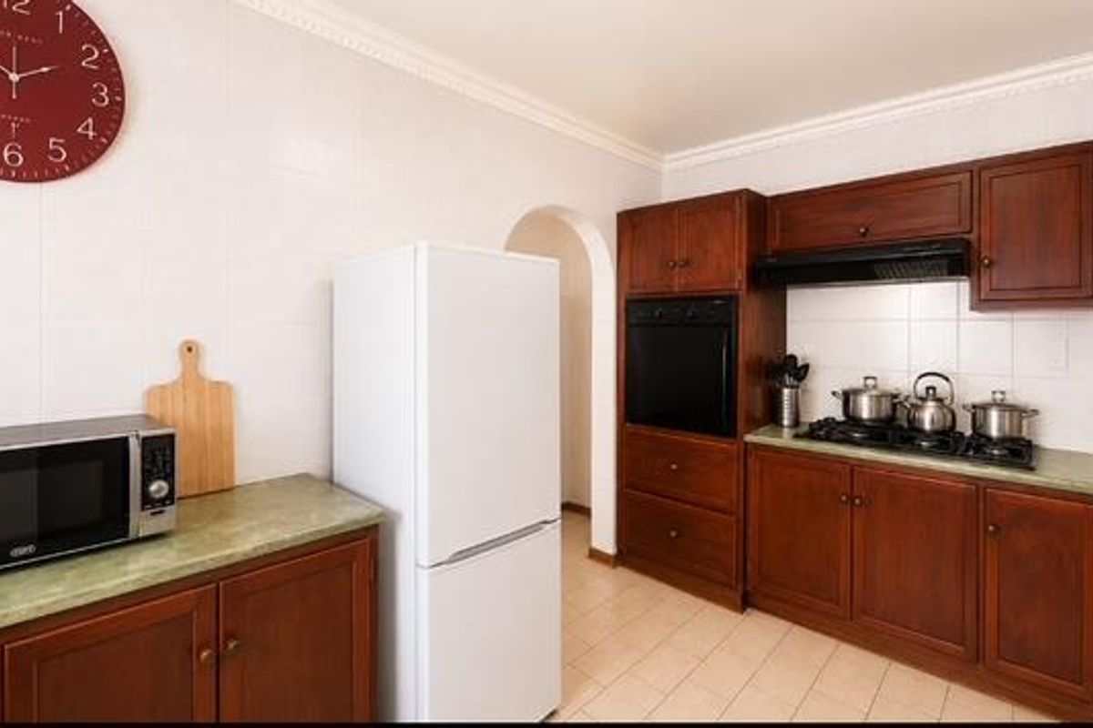A functional kitchen featuring dark wood cabinetry, built-in oven, gas hob with extractor fan, and tiled finishes throughout.