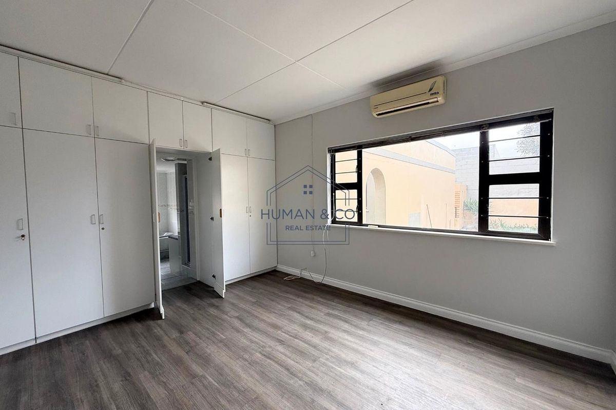 A bright bedroom featuring built-in floor-to-ceiling wardrobes, wood-look flooring, and a wall-mounted air conditioning unit.
