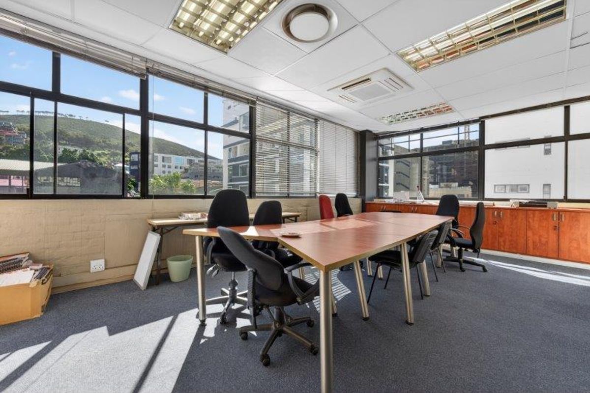 A functional office space featuring large windows with natural light, suspended ceilings with integrated lighting, air conditioning, and built-in storage cabinetry.