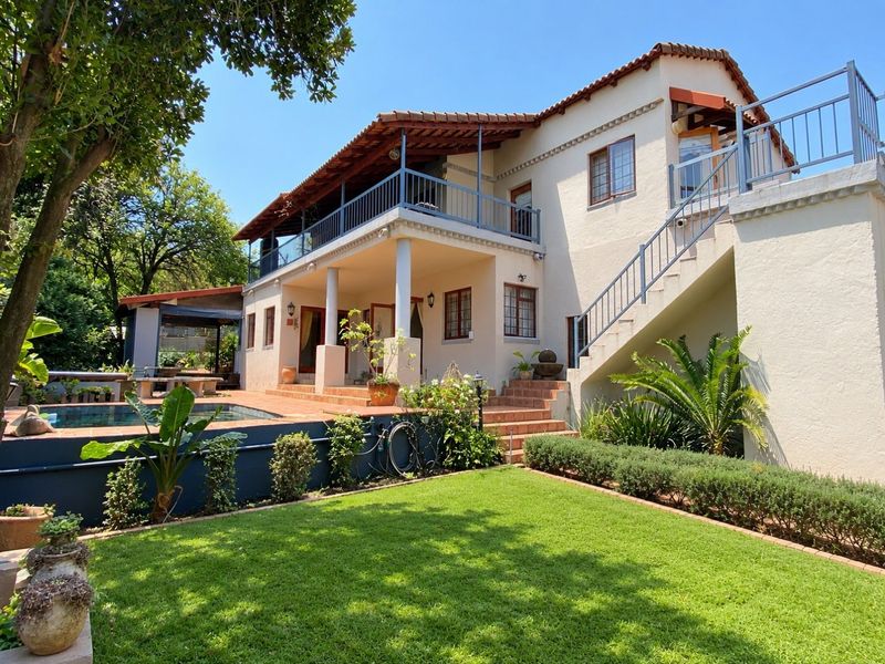 Rear view of the property featuring a swimming pool, covered patio, upper-level balcony, and external staircase set within a landscaped garden.