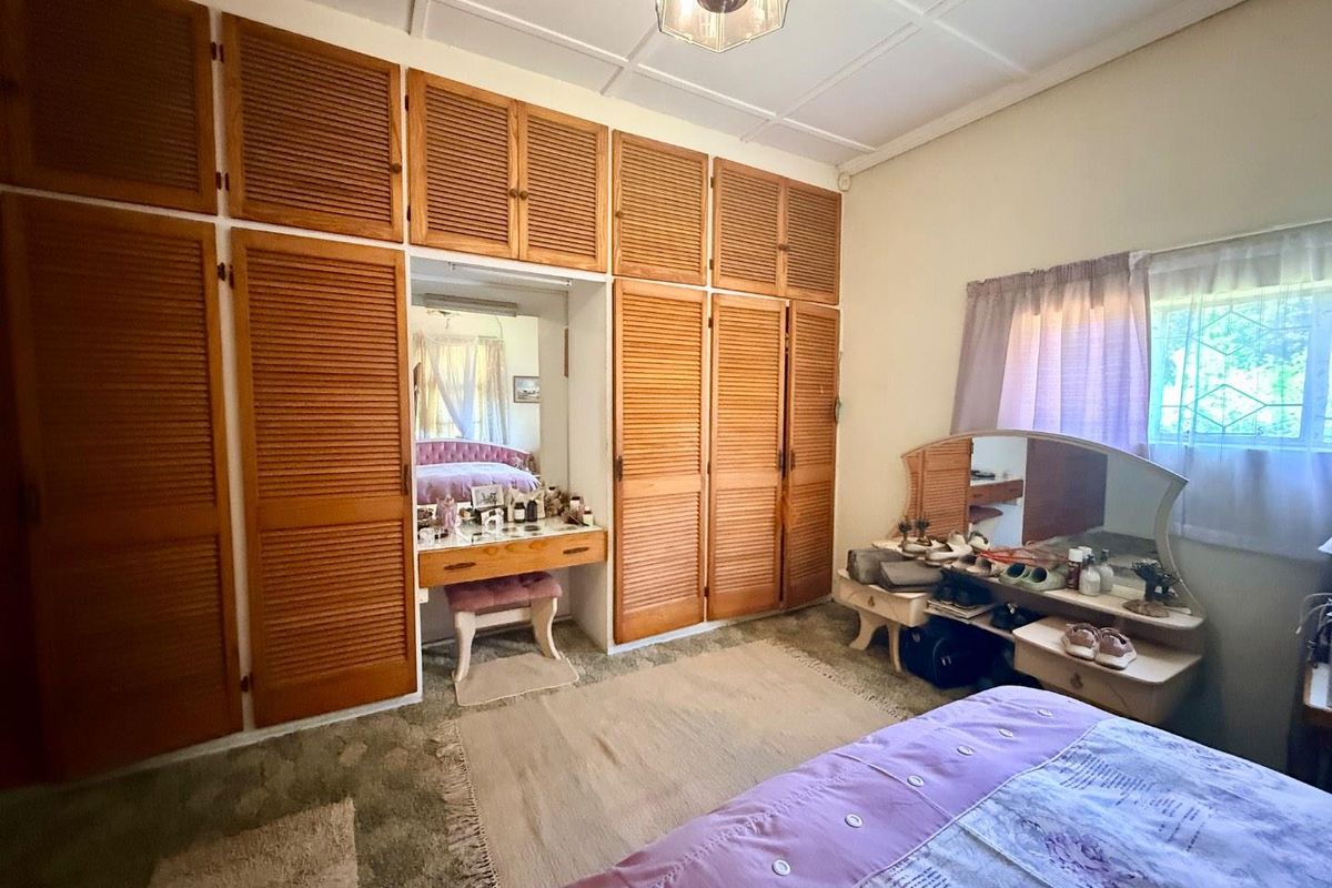 A bedroom featuring extensive built-in wooden louvered wardrobes with an integrated vanity area and large window with security bars.