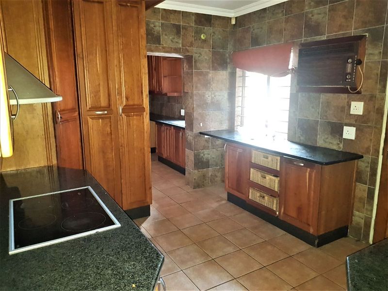 A functional kitchen featuring wooden cabinetry, granite countertops, an electric hob, and tiled finishes throughout, with an adjoining scullery area.