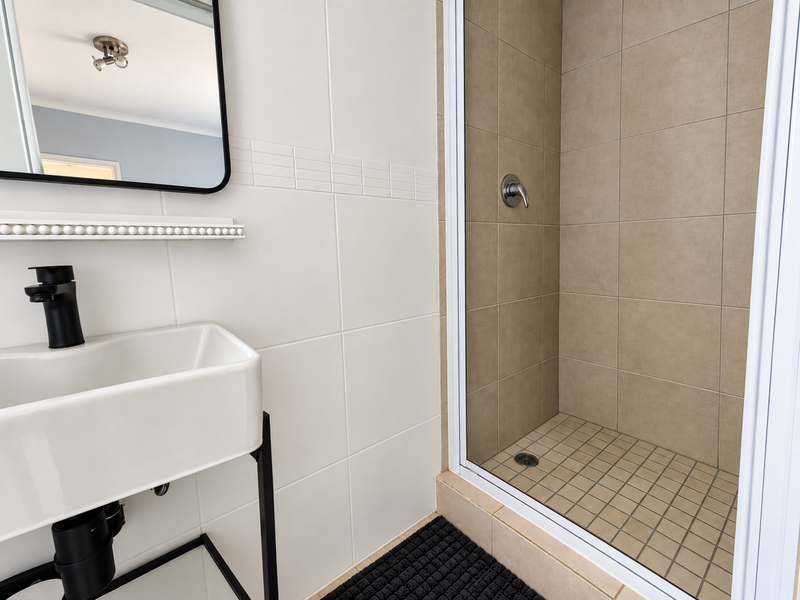 Modern bathroom featuring a wall-mounted basin with matte black fixtures and a separate tiled shower enclosure with a glass door.