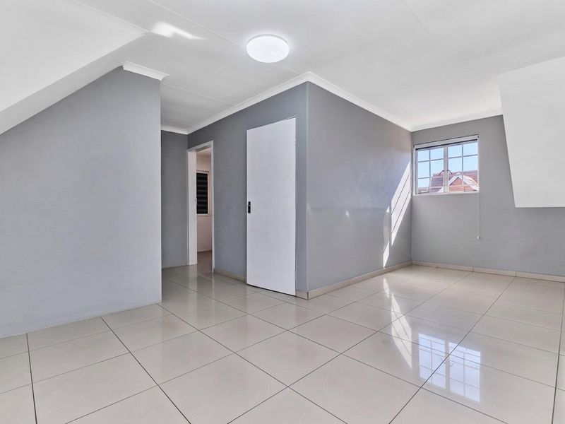 A bright, empty bedroom featuring neutral grey walls, polished floor tiles, and a window with security bars.