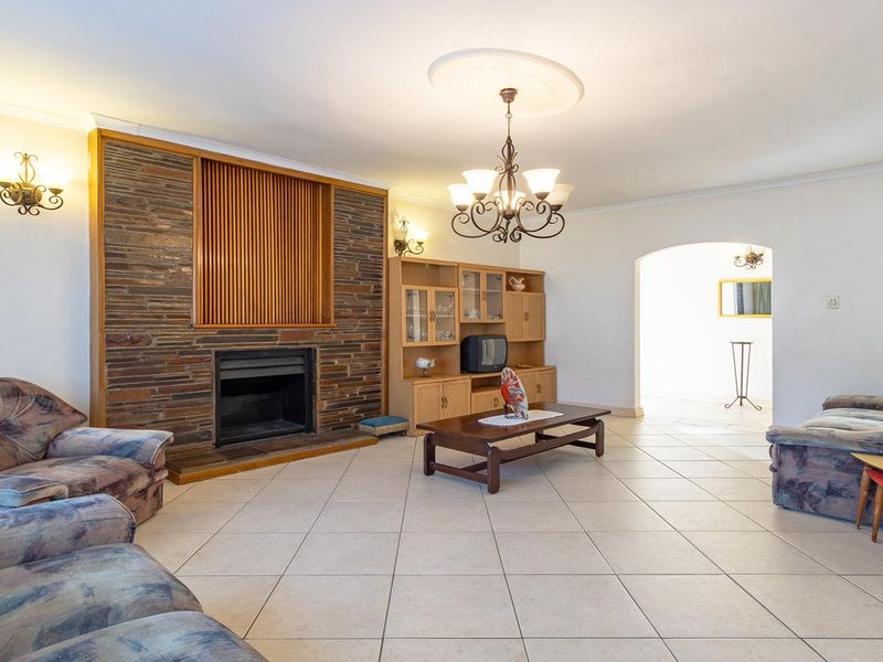 Spacious living room featuring a prominent stone fireplace, tiled flooring, and classic architectural details including a ceiling rose and arched entryway.