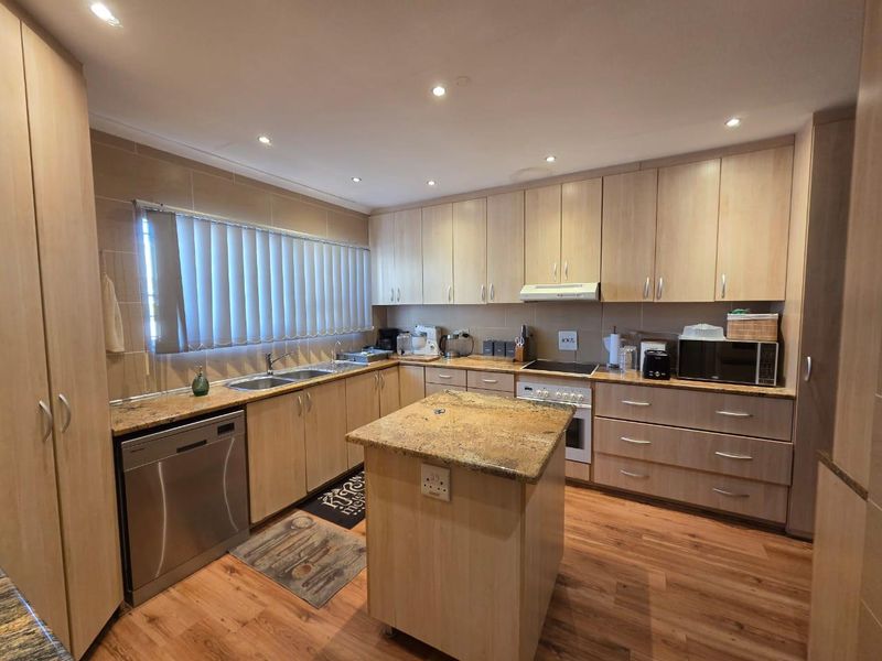 A functional kitchen featuring light wood cabinetry, granite countertops, a central island, and integrated appliances, offering a clean and practical workspace.