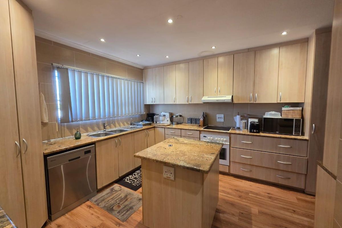 A functional kitchen featuring light wood cabinetry, granite countertops, a central island, and integrated appliances, offering a clean and practical workspace.