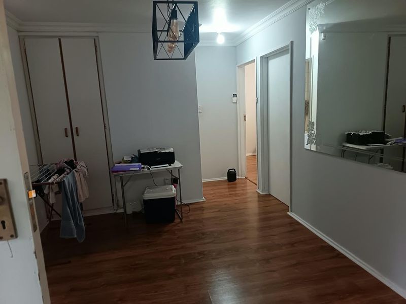 A functional hallway featuring laminate flooring, built-in storage cupboards, and a large wall-mounted mirror, providing access to adjacent rooms.