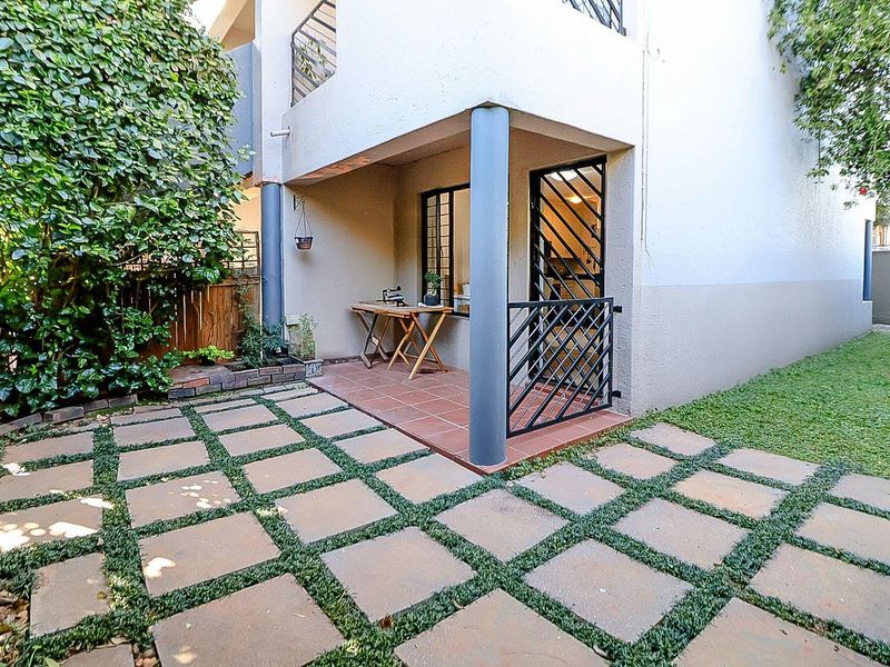 A private rear patio area featuring tiled flooring, structural columns, and a secure metal gate, leading out to a paved garden pathway.