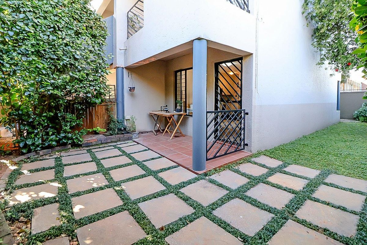 A private rear patio area featuring tiled flooring, structural columns, and a secure metal gate, leading out to a paved garden pathway.